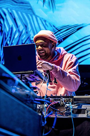 The DJ at ADCOLOR After Dark behind the decks, lit blue against the palm-print screens.