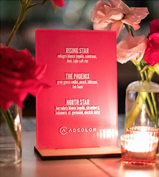 A printed Rising Star cocktail menu card standing on a table beside roses and a candle.