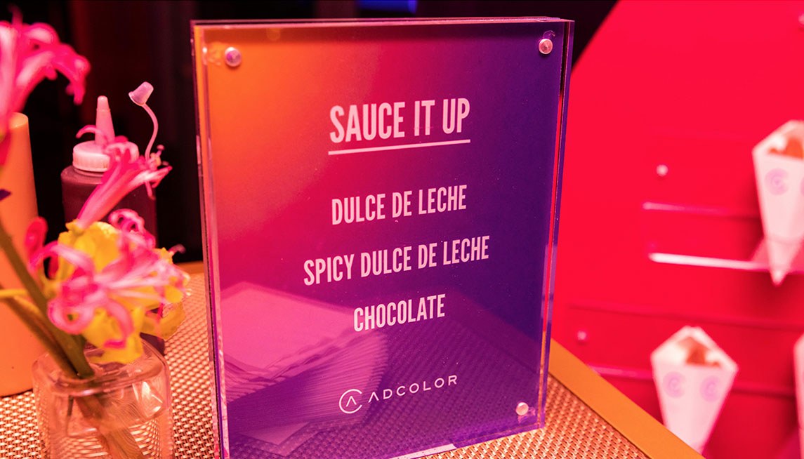 A printed Sauce It Up menu card in an acrylic stand at the dessert station, listing dulce de leche, spicy dulce de leche, and chocolate.
