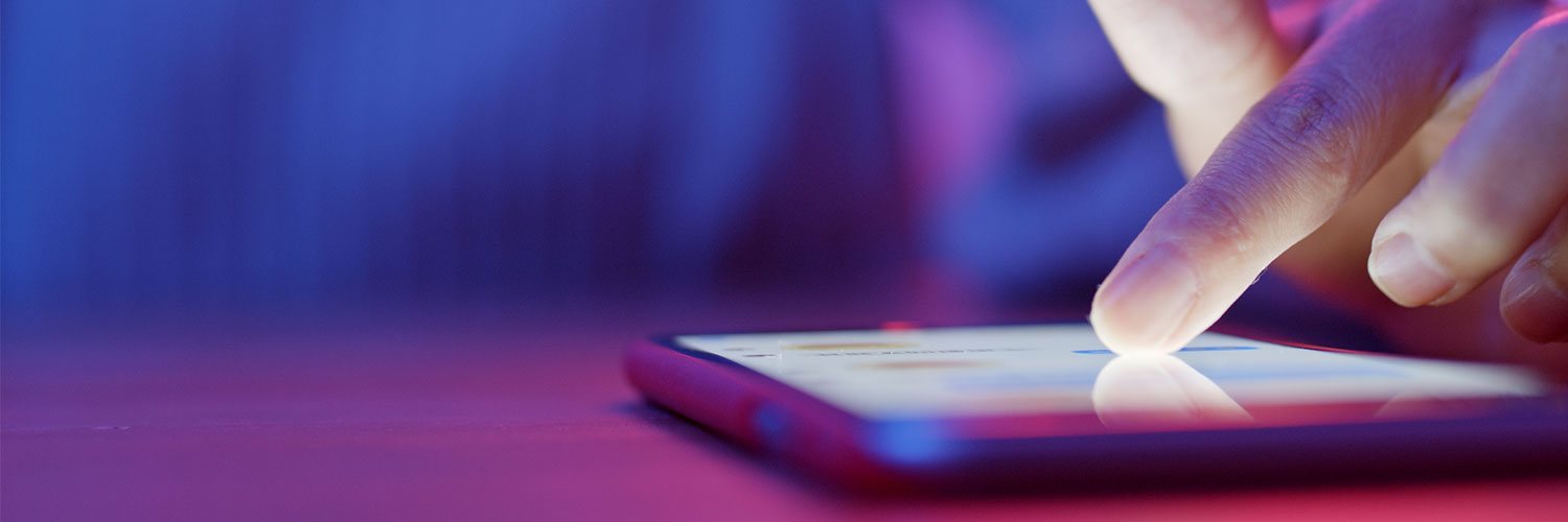 A fingertip tapping a glowing phone screen in dim purple light.
