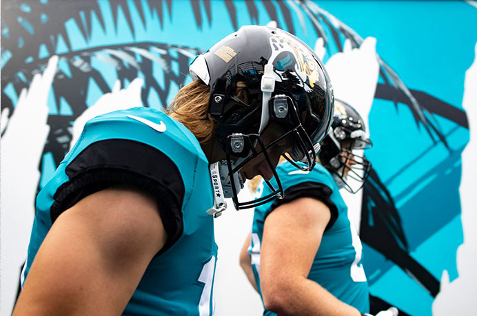 The Jaguars photo treatment: players in helmets emerging against the jungle-texture wall.