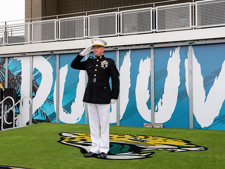 A service member saluting on the field in front of the painted Duuuval wall and the jaguar head.