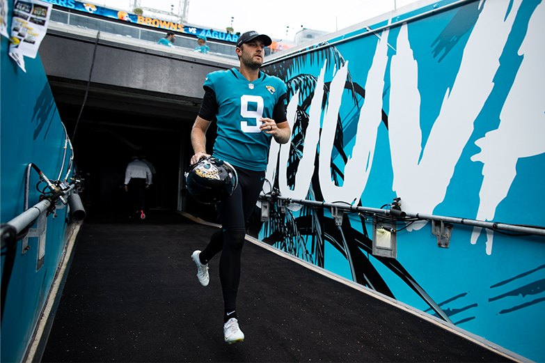 A player walking up the tunnel toward the field, helmet in hand, alongside the painted Duuuval wall.
