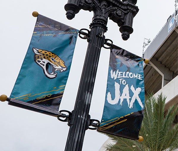A Welcome to Jax street banner pair on a lamp post outside the stadium, carrying the jaguar head and the custom display face.